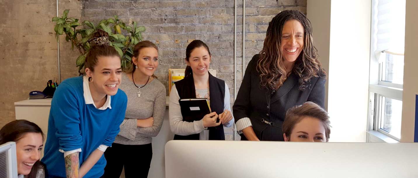 Lashbrook team members gathered around a computer in the studio smiling while looking at the monitor.