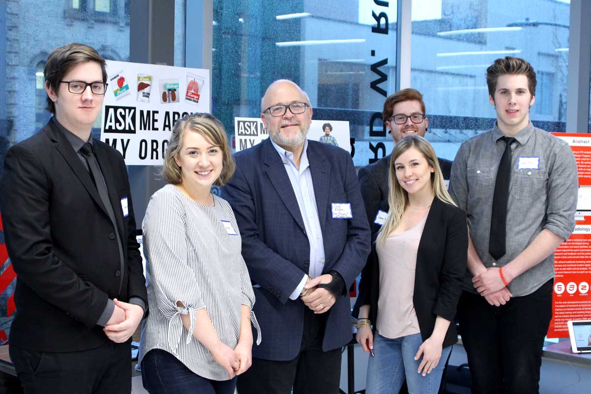 Man posing for a photo at Fanshawe College’s downtown campus with five students from the interactive media and design program. 