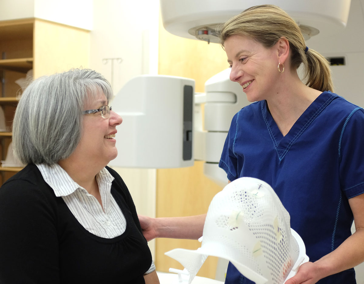 Female nurse helping a female patient with glasses stand up. 