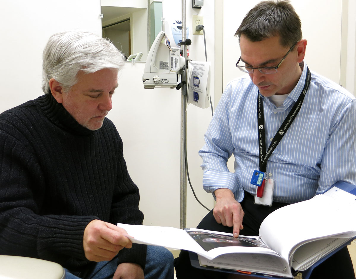 Male physician pointing to a photo in a book with a male client beside him.