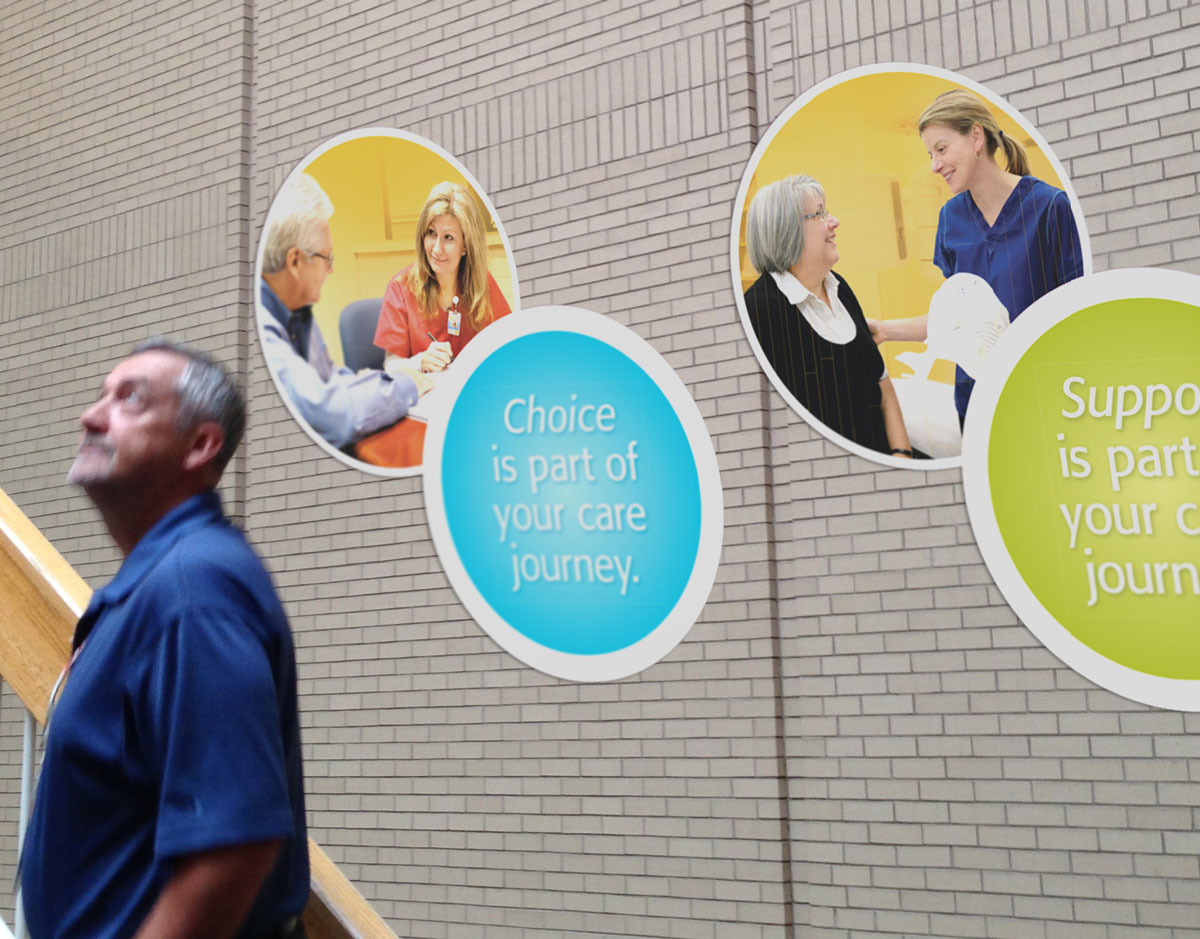 Male looking up at multiple circle decals on a brick wall with patient and nurse photos on them.