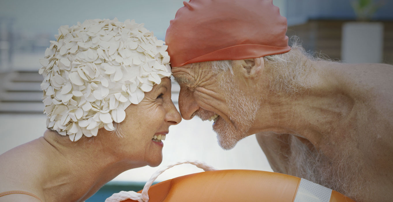 Female and male looking in each other’s eyes, wearing swim caps, while holding a ring buoy.